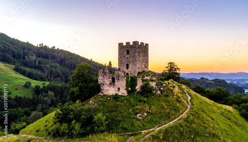 A stone structure crowns a verdant hilltop. Rolling hills recede into the distance under a warm sunset, creating a picturesque scene