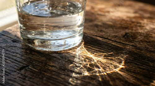 Water glass with sunlight reflection on wooden table
