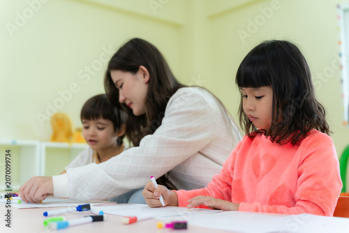 Focused little Asian girl drawing with markers during an art lesson in kindergarten classroom.