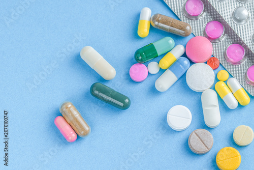 Scattered colorful medical pills capsules and tablets next to blister packs on blue background