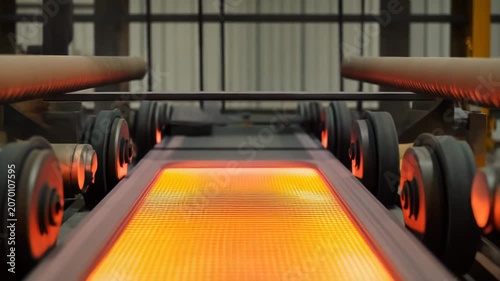Hot orange hot steel slab glowing as it travels on a conveyor through a steel mill, showcasing high temperature industrial production, heavy machinery and automated workflow