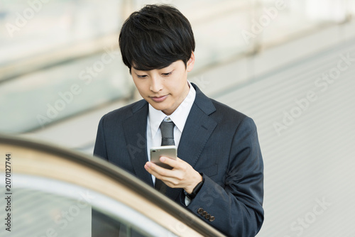 エスカレーターでスマートフォンを使う20代男性ビジネスマン