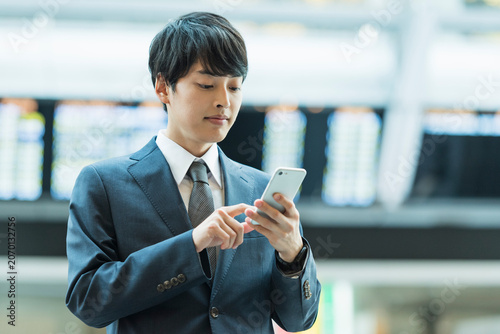 Foto 駅のコンコースでスマートフォンを操作する20代男性ビジネスマン
