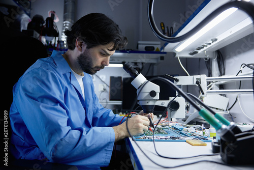 A technician working on circuit board under microscope in lab