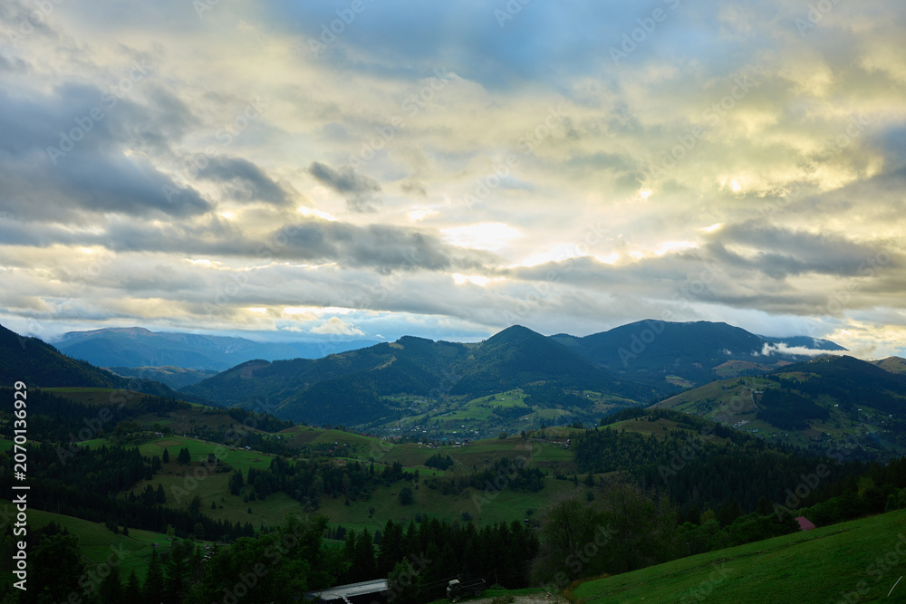 Obraz premium Thick clouds fill the sky over the Carpathian Mountains. Green trees are visible below with fog rolling over the landscape. It appears cold on this cloudy autumn day in Ukraine.