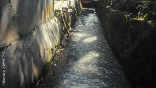 Flowing Gray Water In A Concrete Drainage Canal With Sunlight Reflections And Shadows On The Wall