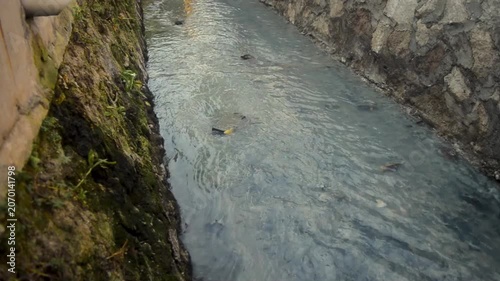 Dirty Water Flowing Through Concrete Drainage Channel With Stone Walls and PVC Pipe Outlet