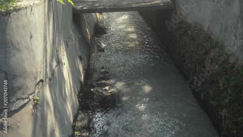 Concrete Drainage Canal With Flowing Water And Sun Reflections In An Urban Setting