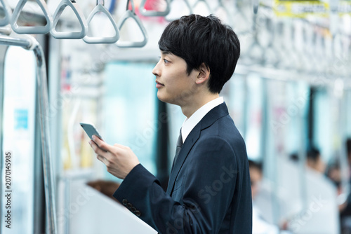 Foto 電車内でスマートフォンを操作する20代男性ビジネスマン