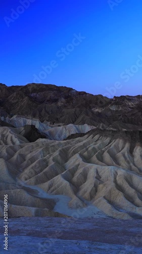 Vertical Screen: Zabriskie Point in Death Valley National Park California displays dramatic eroded mudstone badlands during blue hour with deep shadows accentuating the rippled sedimentary formations.