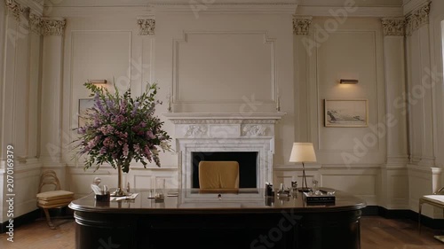 Empty elegant executive office with a large dark wood desk, antique armchair, blooming floral arrangement, and classic architectural details reflecting professional corporate style