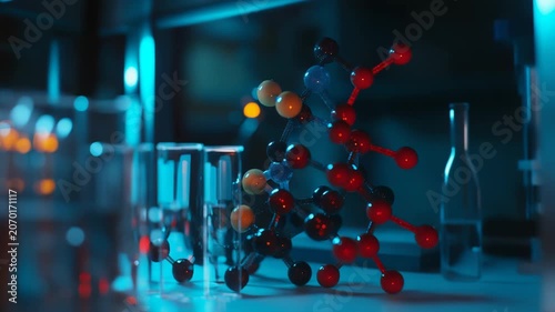 Molecular model with colorful atoms and connecting bonds standing next to glass test tubes in a dimly lit laboratory, symbolizing scientific research, biotechnology, and chemical analysis