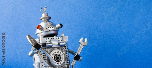 Fotografía Unusual metallic robot handyman with multicolored eyes gripping pliers and wrench, blue backdrop text placeholder