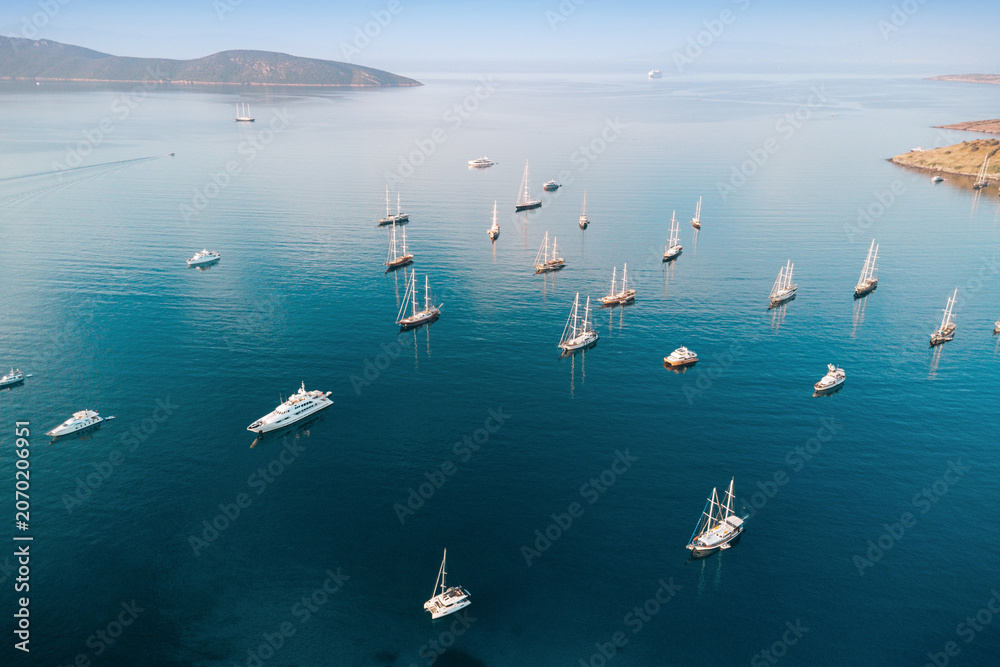 Obraz premium Aerial view of luxury yachts, sailboats, and gulets in a serene bay, capturing summer travel and relaxing holidays in blue waters