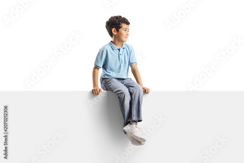 Young boy sitting on a white panel and looking away to the side