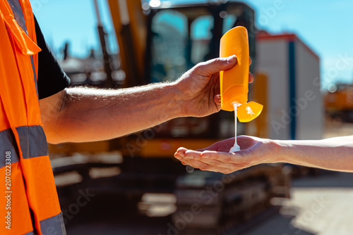 Tableau sur toile Bauarbeiter spritzt Sonnencreme auf eine Hand