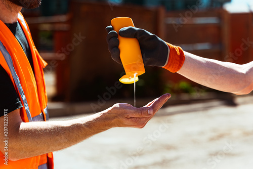 Bauarbeiter spritzt Sonnencreme auf eine Hand