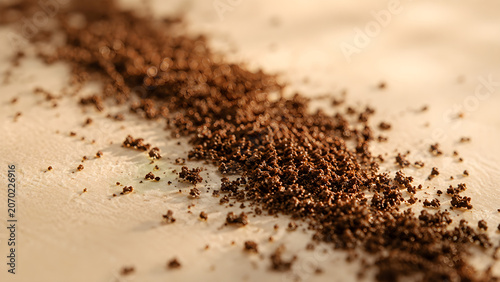 Dark granular vanilla powder scattered on a beige surface