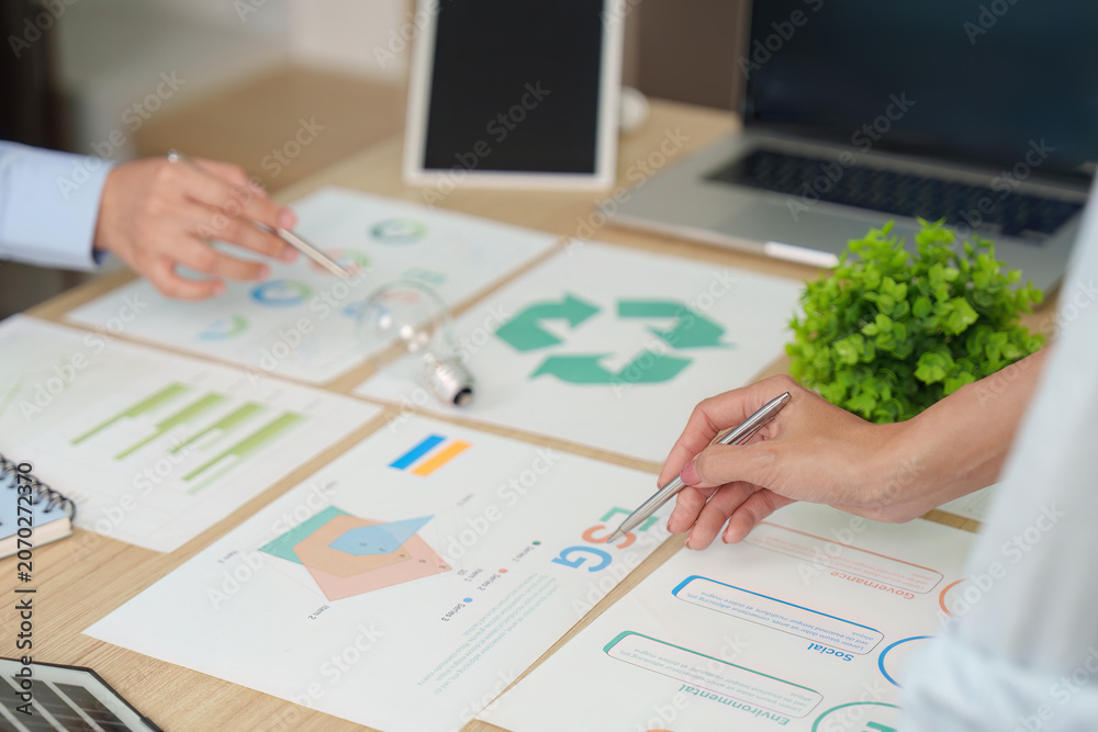 Fototapeta premium Cropped hands of businesspeople analyzing ESG charts for corporate sustainability strategy