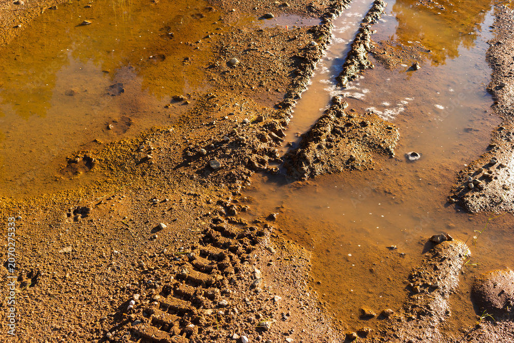 Naklejka premium Deep tire tracks from an enduro motorcycle carved into the wet sandy soil of a quarry with muddy puddles, showcasing intense off-road adventure and challenging riding conditions