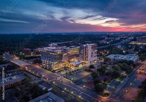 Reston, Virginia, United States - 27 May 2020: Aerial view of modern office buildings and residential complexes illuminated at dusk under a vibrant sunset sky.