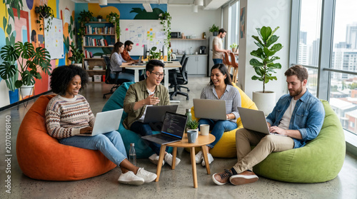 Multicultural coworkers using laptops while seated on colorful bean bags in a modern open office, with plants, collaborative desks, bright windows, creative wall art, and an energetic work setting