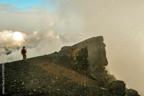 Hiker Standing on the Volcanic Rim above the clouds on a foggy day in the Alpine Desert Zone of Mount Meru, Arusha National Park, Tanzania