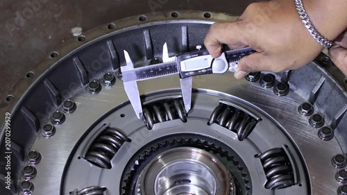 Close-up of a mechanic's hand using a digital vernier caliper to check the clearance or size of a damper spring inside an automatic transmission torque converter assembly.