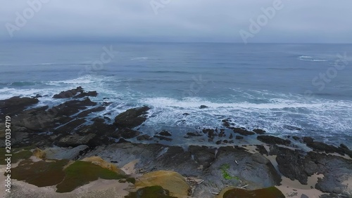 Fotografía Rocky coastline with waves crashing against dark rocks in ocean