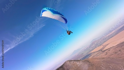 Paraglider flying over dry mountain landscape at sunset