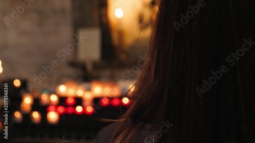 Rear view of a woman standing inside a church and looking toward burning prayer candles. Spiritual reflection, Christian faith, worship, prayer, hope, devotion and religious traditions concept. High