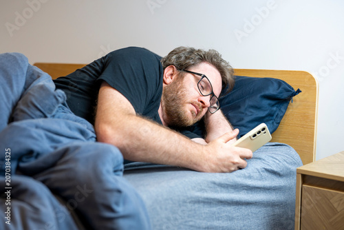 Photos Man lies in bed, scrolling phone