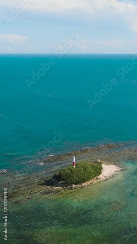 Aerial drone of rocky island with a lighthouse in the blue sea. Borneo, Malaysia. Vertical video.