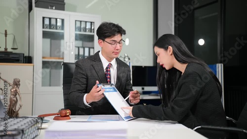 Professional Asian attorney explains legal contract terms to a businesswoman, leading to a successful deal and handshake in a modern law office workspace.