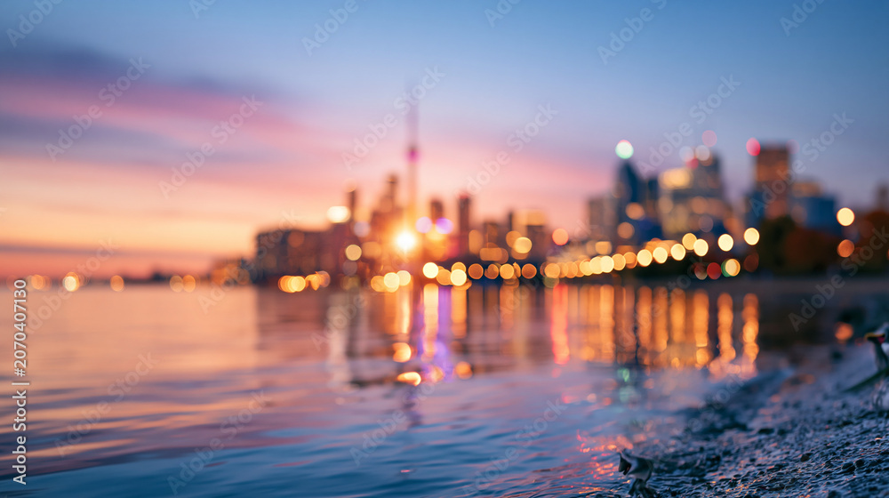 Fototapeta premium A wide shot of a sweeping calm city skyline glowing softly across the bright water from a distant viewpoint city skyline faceless scene softly defocused backdrop bright