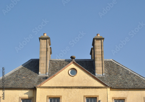 Facade Pediment and Chimney Stacks of Early 19th Century Stone Building seen against Blue Sky 