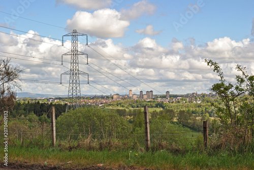 View Across Fields to Power Pylon and Distant Town on Sunny Day 