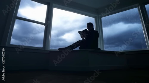 Silhouetted person reading on windowsill during stormy overcast middle sequence showing