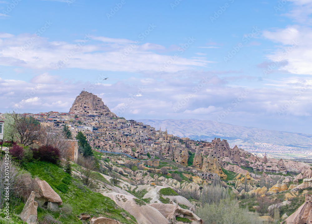 Obraz premium A scenic view of the historic Uchisar Castle and unique fairy chimney rock formations in the Cappadocia region of Turkey under a blue sky.