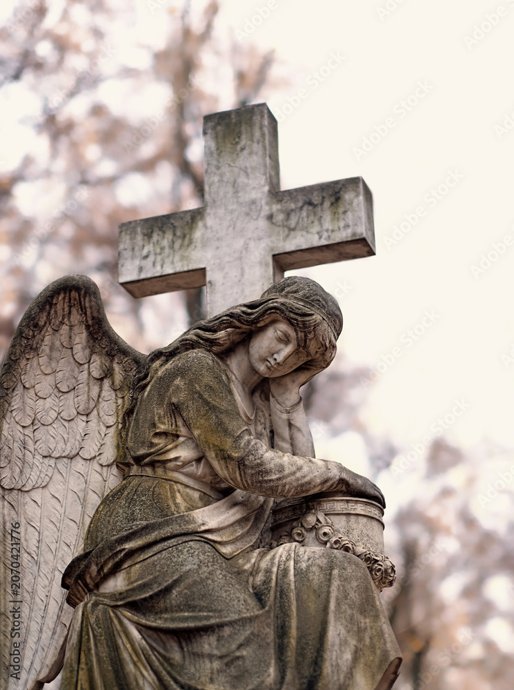 Fototapeta premium fragment old monument of angel with cross on cemetery. symbol of religion, faith in God, resurrection, memory, eternity. all saints day. Design for condolences, mourning card, obituary.