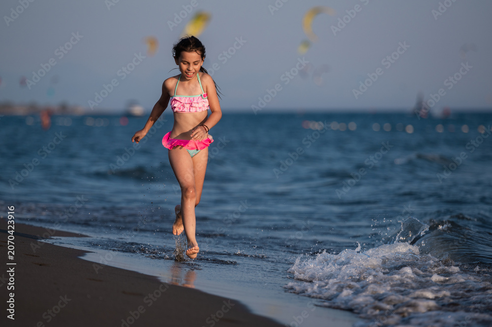 Fototapeta premium Happy girl running along beach shoreline with ocean waves