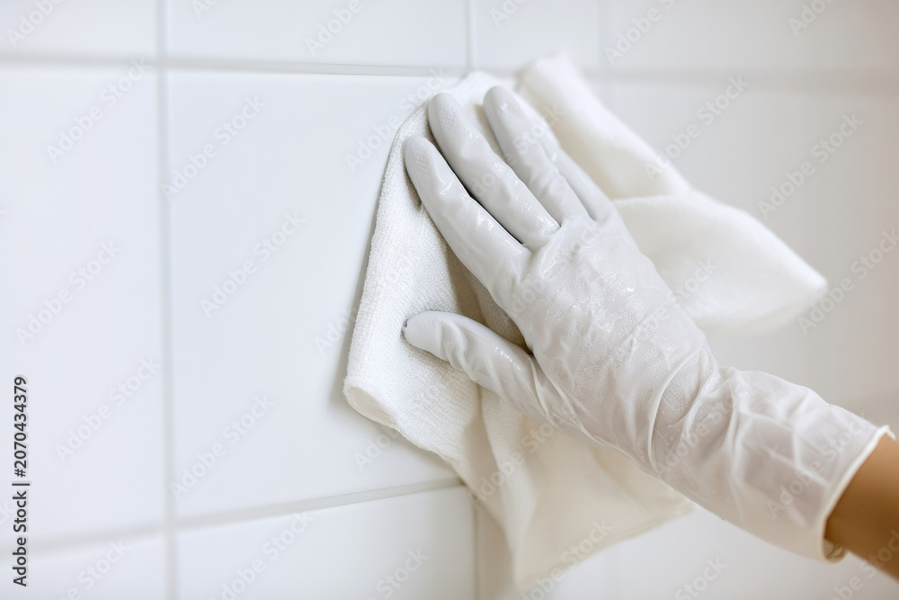 Fototapeta premium Bathroom tile grout cleaning, gloved hand wiping ceramic tile with microfiber cloth in bright modern bathroom with soft light and copy space
