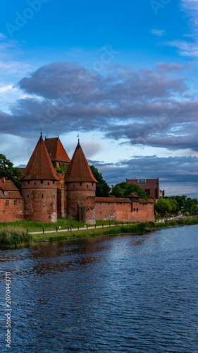 Vertical view of historic Malbork Castle towers under dramatic cloudy sky in Poland