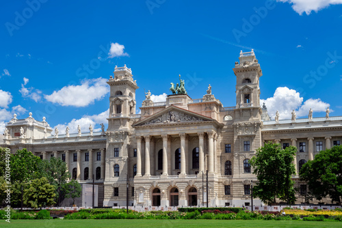 Detailed exterior view of the historic Hungarian Parliament Building in Budapest, Hungary, featuring its iconic dome, ornate facade and Neo-Gothic spires beneath a bright blue sky.