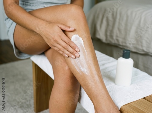 Woman applying moisturizing lotion to her leg, body care routine at home.