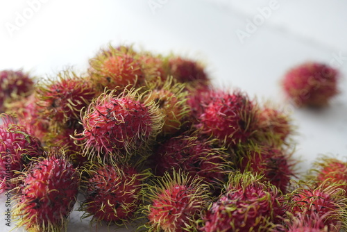 Fresh rambutans with vibrant red and pink skins are arranged together on a light background, showcasing their distinctive greenish-yellow soft spines. This image represents tropical freshness, natural