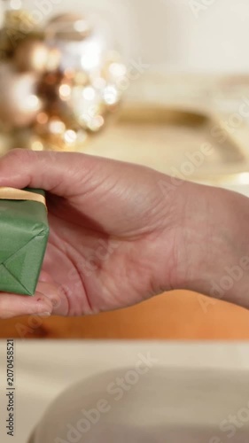 Vertical video: Holding right hand rotating and releasing green gift on wooden table with ornaments