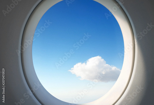 View through airplane porthole window of white fluffy cloud in clear blue sky during flight with airplane aviation porthole transport aircraft
