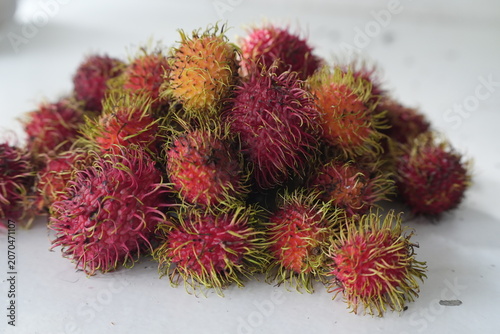 Fresh rambutans with vibrant red and pink skins are arranged together on a light background, showcasing their distinctive greenish-yellow soft spines. This image represents tropical freshness, natural