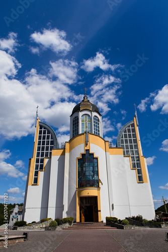 Modern Cathedral of Saints Peter and Paul in Chortkiv, featuring contemporary church architecture, large windows, a central dome, and a dramatic blue sky.